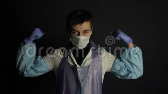 一位穿着保护性医疗服的白种人医生显示了他的二头肌力量黑色的黑暗背景支助视频的预览图
