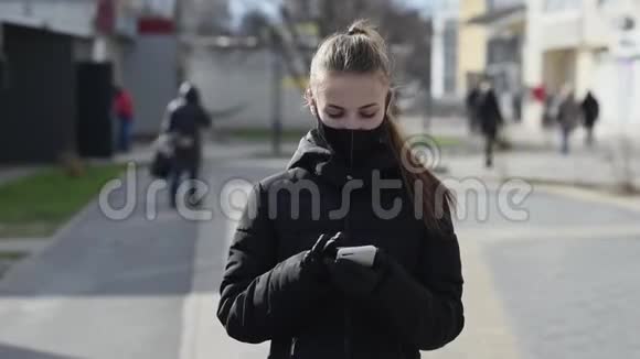 戴防护面罩和手套的女孩在户外使用智能手机COVID19世界冠状病毒大流行视频的预览图