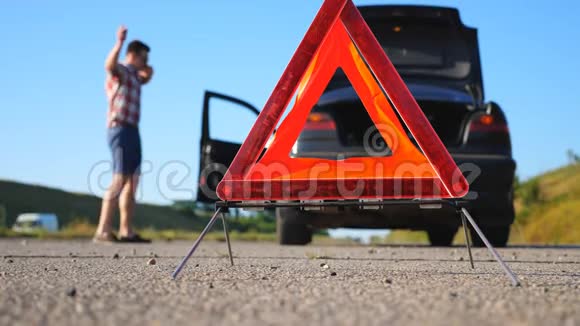 关闭站在道路上的红色紧急停车标志担心和愤怒的司机走在他的破车附近谈论着视频的预览图