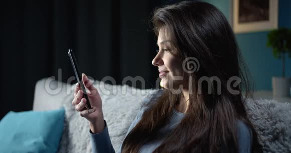 快乐的女人在沙发上使用智能手机视频的预览图