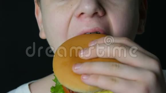 一个十几岁的男孩的嘴他吃两个多汁的汉堡一个芝士汉堡或汉堡里面有奶酪肉切片和泡菜视频的预览图