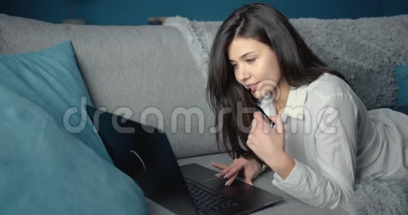 可爱的女人在沙发上用笔记本电脑放松视频的预览图