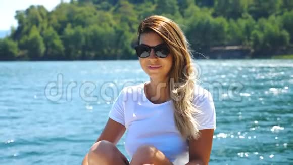 快乐的金发女郎坐在游艇上漂浮在海湾的肖像背景是美丽的景色青年视频的预览图