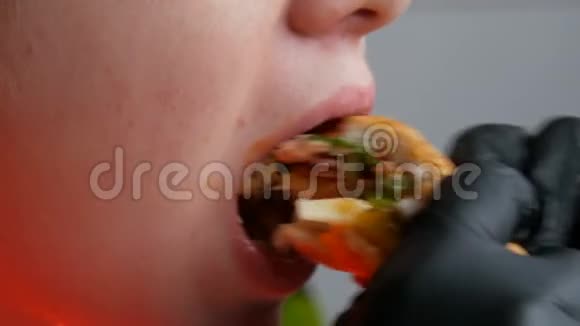 一个十几岁的孩子吃了一个大的多汁汉堡里面有一个鸡蛋一个西红柿沙拉和红酱双手戴黑色手套视频的预览图
