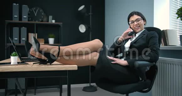 漂亮的女商人在电话里说话腿放在桌子上视频的预览图
