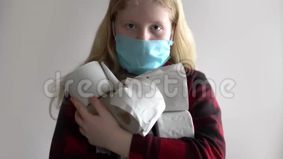因冠状病毒流行而被隔离戴面具的女孩在灰色背景上摆着一卷卫生纸视频的预览图