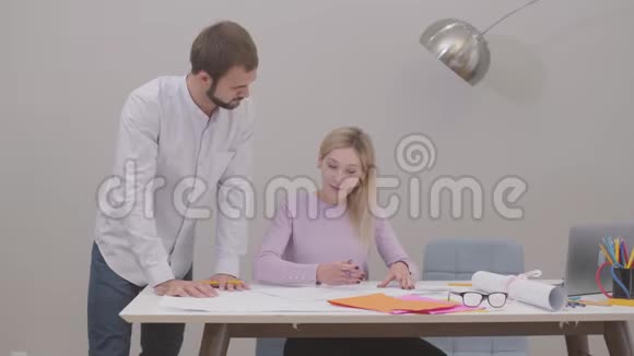 长胡子的白种人男子站在桌子旁边看着他的助手的图纸年轻女设计师视频的预览图