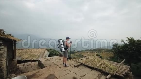 一位年轻的白种人游客从山上拍摄尼泊尔梯田稻田背包尼泊尔村庄视频的预览图