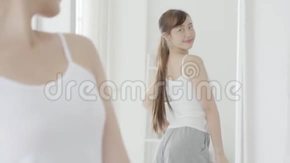 美丽的肖像亚洲年轻女子微笑着穿衣看着卧室的镜子视频的预览图