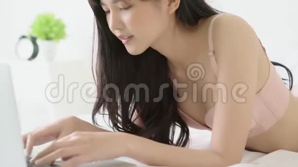 美丽的年轻亚洲性感女人兴奋地用手提电脑上网躺在房间的床上视频的预览图