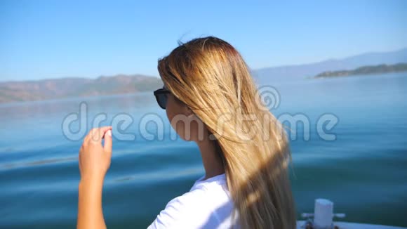 金发女郎坐在游艇上漂浮在平静的大湖表面享受自由的年轻女孩视频的预览图