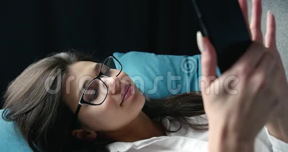 黑发女人在沙发上用智能手机发短信的肖像视频的预览图