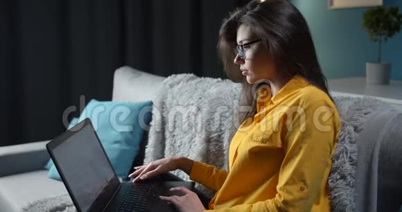 黑发女人坐在沙发上用电脑侧视视频的预览图