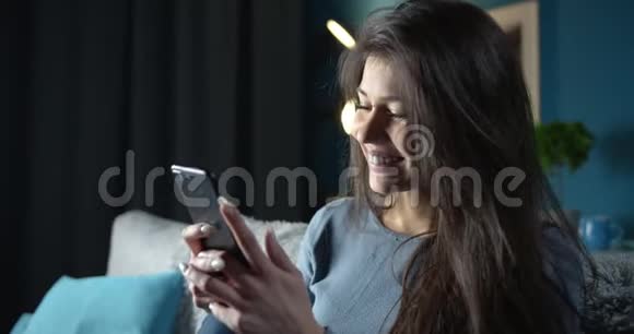 年轻漂亮的女士在沙发上用智能手机发短信视频的预览图