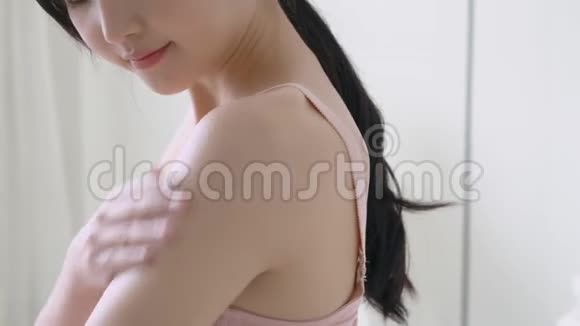 美丽的年轻亚洲女人微笑着在卧室里涂防晒霜乳液视频的预览图