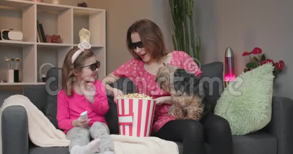 快乐的高加索女人和她戴着3D眼镜的小女儿坐在沙发上一边在电视上看喜剧电影视频的预览图
