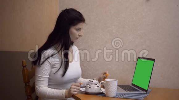 年轻女性在厨房里用绿色屏幕的笔记本电脑工作喝咖啡视频的预览图