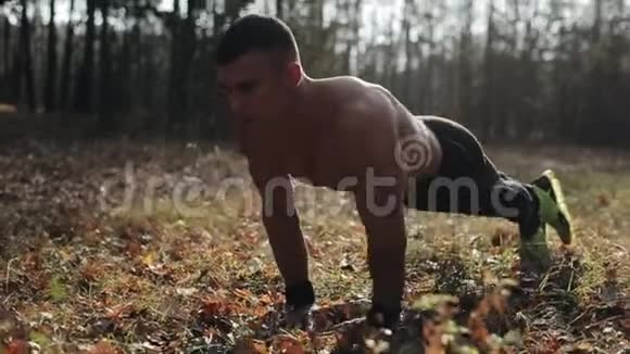 年轻的肌肉运动员在森林里做俯卧撑强壮的白种人赤裸的躯干视频的预览图