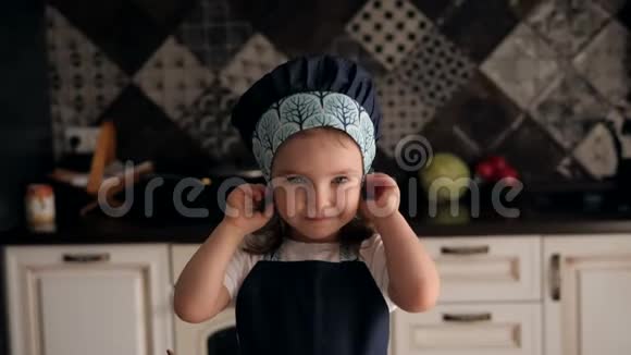 厨房里一个戴着帽子和围裙的4岁小女孩的肖像视频的预览图