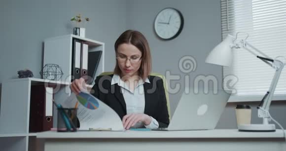 自信的年轻女商人在工作场所使用财务文件和电脑打字视频的预览图
