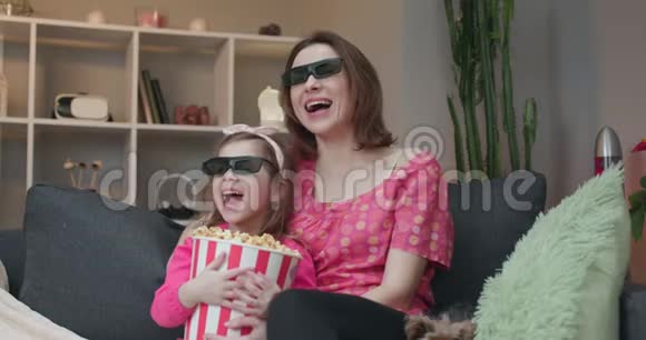 女人和一个小女孩戴着3D眼镜看电视和吃爆米花家庭时间和年轻女孩放松视频的预览图