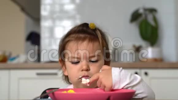 蹒跚学步的小女孩用勺子在厨房里吃午饭脏手视频的预览图