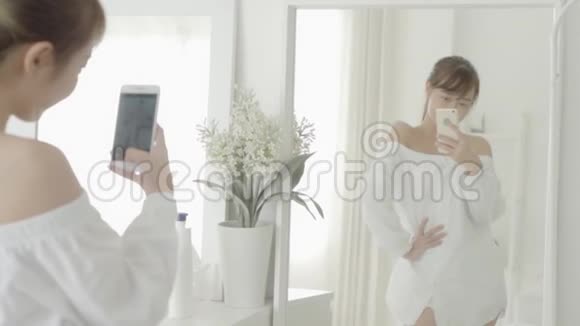 漂亮的亚洲年轻女性在客厅里用智能手机照镜子自拍视频的预览图
