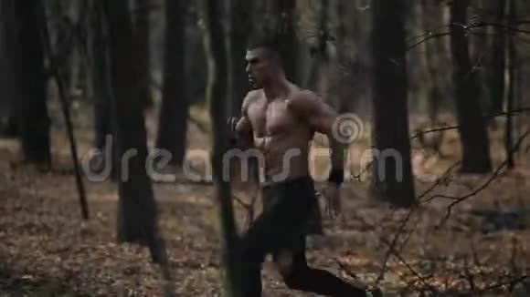 年轻的肌肉运动员在森林里奔跑在树之间奔跑慢动作视频的预览图