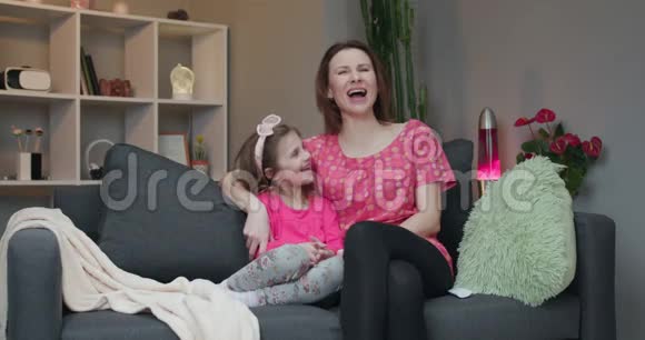 女人和她的小女儿坐在沙发上在电视上看喜剧电影笑视频的预览图