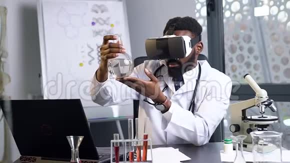 有目的的35岁留胡子的非裔美国男医生用虚拟现实技术用化学液体看瓶子视频的预览图