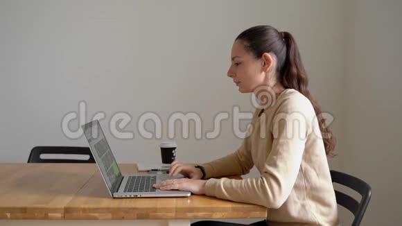 年轻的女人在家里用笔记本电脑在木桌上工作工作日结束视频的预览图
