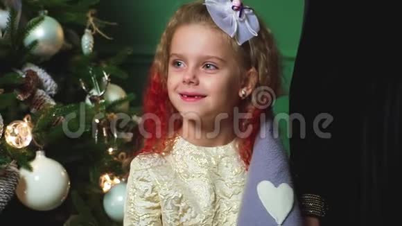 一个美丽的小女孩在一棵装饰着的圣诞树的背景上挂着灯视频的预览图