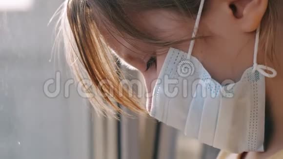 检疫威胁冠状病毒悲伤的孩子戴着防护医疗面具坐在窗台上看着窗外病毒视频的预览图