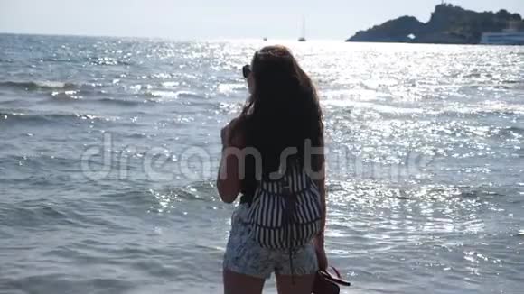 女旅行者站在海边欣赏美丽的海景年轻女孩背着背包享受风景视频的预览图