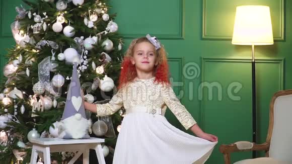 一个美丽的小女孩在一棵装饰着的圣诞树的背景上挂着灯视频的预览图