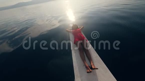 一个女人躺在帆船的边缘在海里享受日出视频的预览图