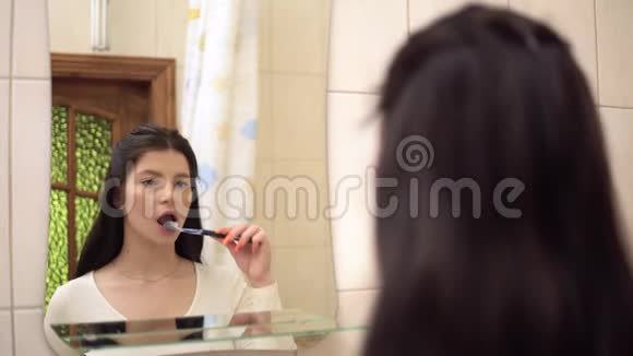 年轻女子刷牙牙膏浴室里的镜子口腔卫生视频的预览图
