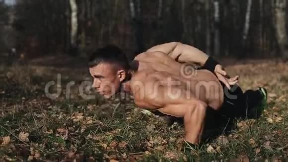 肌肉发达的年轻运动员在森林里用一只手臂做俯卧撑强壮的白种人赤裸的躯干视频的预览图