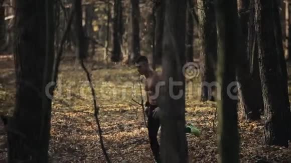 年轻的肌肉运动员赤裸的躯干穿着跑步裤在森林里奔跑在树之间奔跑的速度慢慢视频的预览图