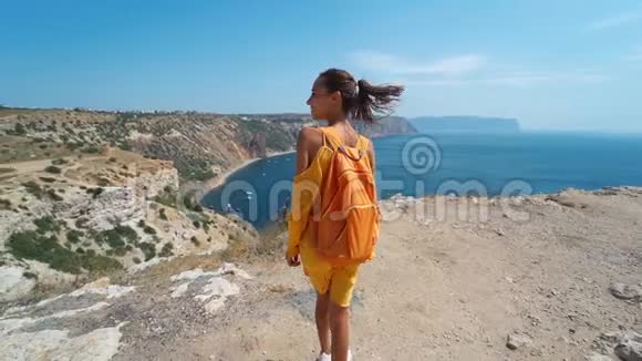 黝黑的旅人女子站在悬崖边的后景身着鲜艳的黄色连衣裙在风中飘扬视频的预览图
