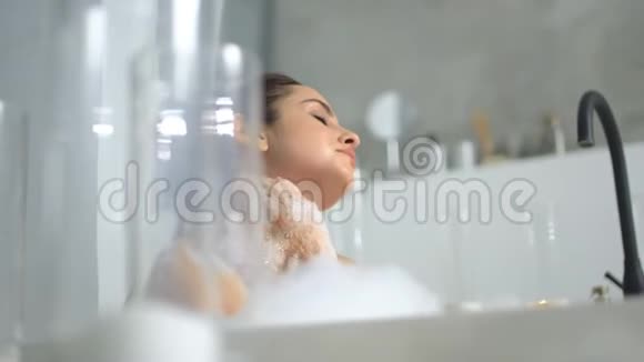 放松的女人在浴缸里按摩脖子关闭性感女孩在洗澡放松视频的预览图