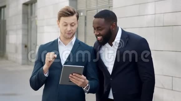 商人们在街上的平板电脑上收到好消息商业伙伴拥抱视频的预览图