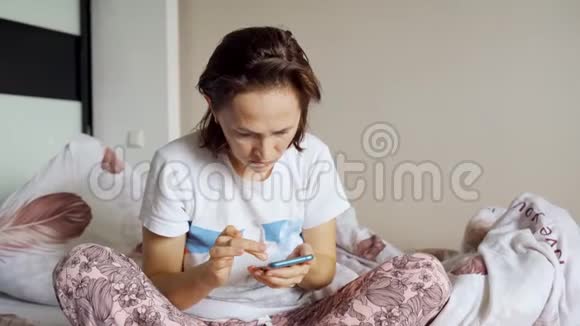 一个穿睡衣的女人坐在一个挺直的沙发上手里拿着一部智能手机视频的预览图