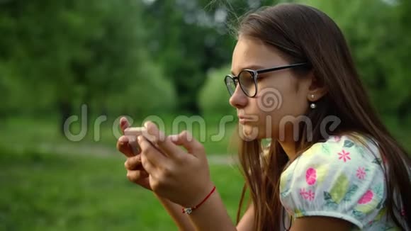 在夏季公园里关闭在智能手机上发短信的严肃女孩视频的预览图