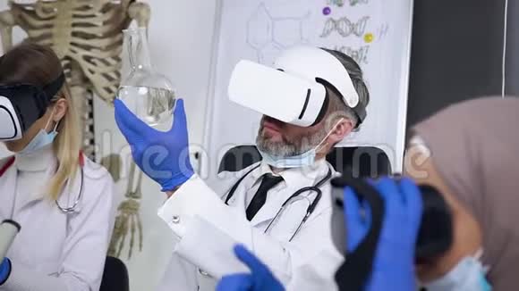 尊敬的灰胡子医生用虚拟现实耳机学习烧瓶中的化学物质视频的预览图