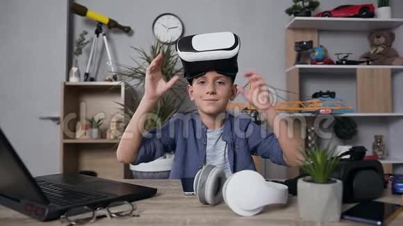 可爱的微笑少年看着相机戴着虚拟现实耳机玩电子游戏视频的预览图
