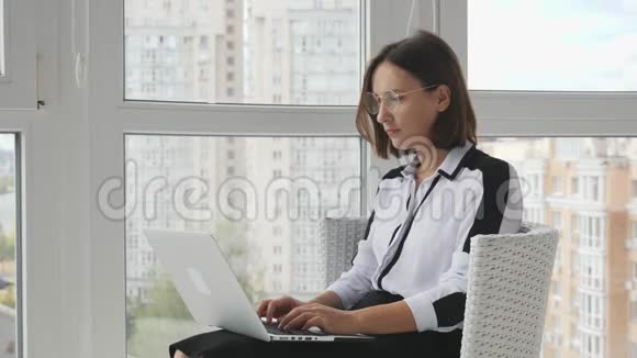 年轻的女商人集中精力穿着白色上衣黑色裙子和太阳镜坐在现代电脑上打字视频的预览图