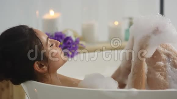 特写性感女人在浴缸里玩泡沫躺在浴缸里的轻松女孩视频的预览图