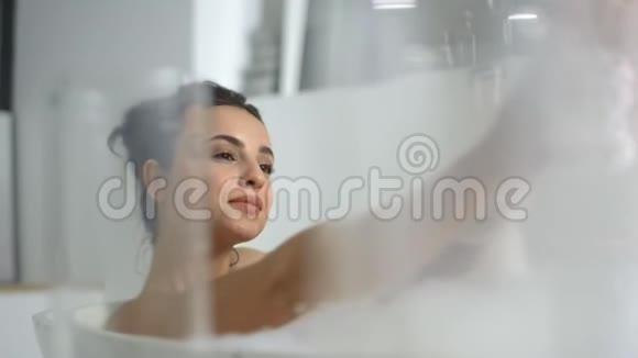 性感的女人躺在浴室的浴沫里浪漫的女孩在浴缸里放松视频的预览图