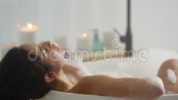 合上躺在浴沫里的轻松女人在浴缸里放松的浪漫女孩视频的预览图